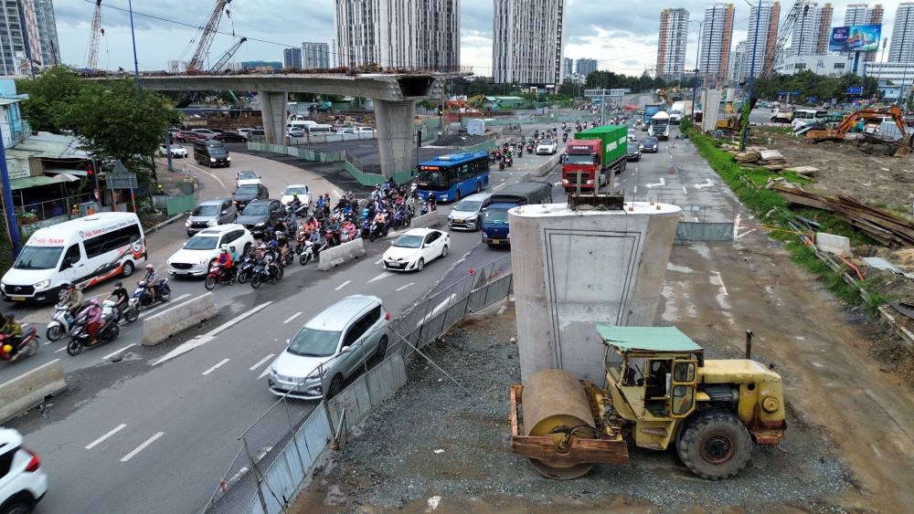 Nhìn từ trên cao, công trường vẫn còn nhiều đoạn im ắng, vắng bóng công nhân. Xen kẽ giữa khối bê tông, thép dở dang là cảnh tượng hỗn loạn giao thông bên dưới. Càng gần mốc về đích, áp lực tiến độ càng đè nặng, trong khi thực tế thi công vẫn ì ạch.